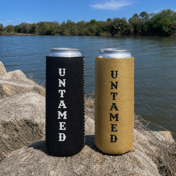 Two can coolers labeled 'UNTAMED' on a rock by a body of water.