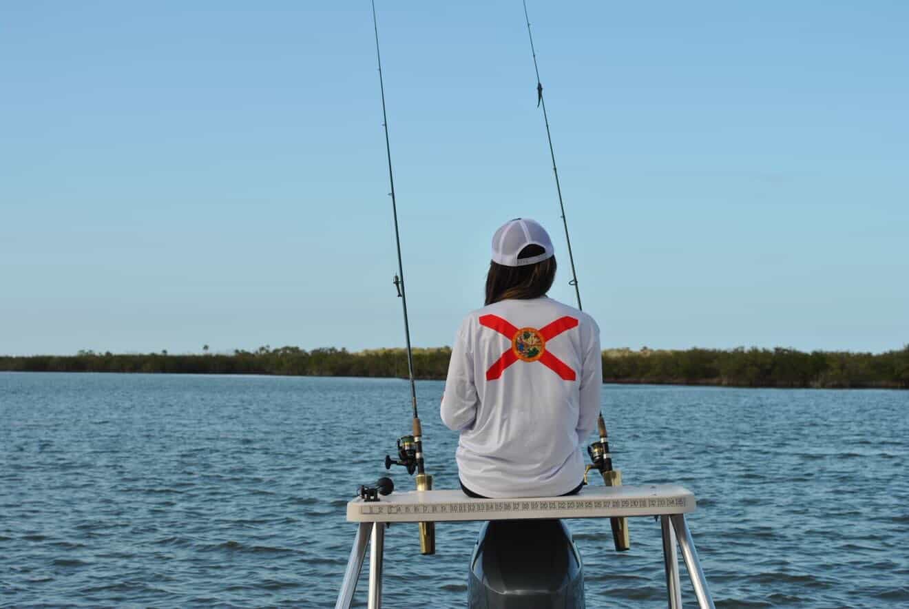 woman fishing on a boat with a Florida flag shirt, surrounded by water and clear sky.